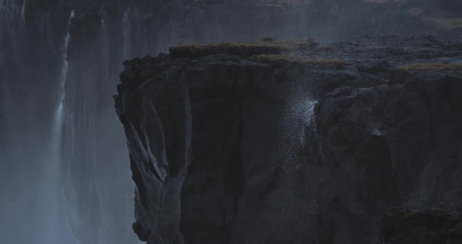 Mist from distant waterfalls drifts over a dark cliffside canyon