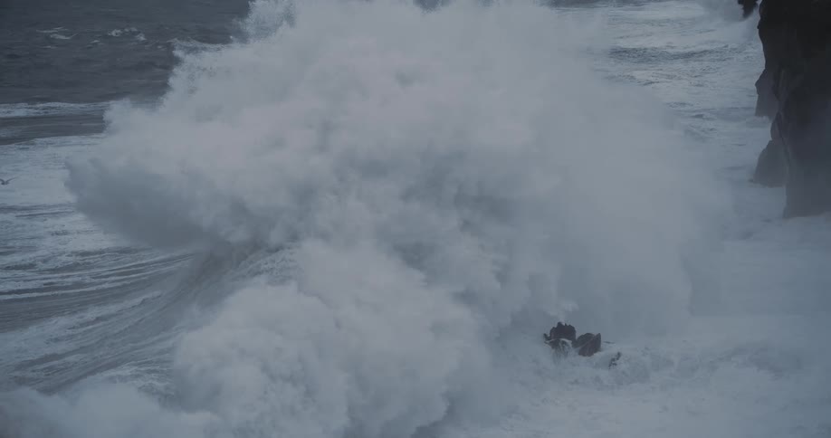 Ocean waves violently crashing against the rocky cliff on the shore at midday