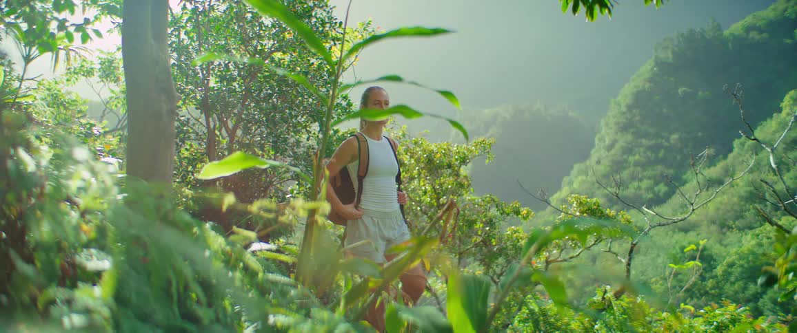 A woman hikes through a lush green mountain trail