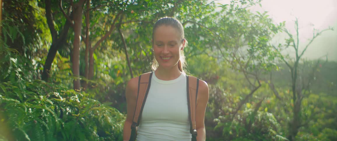 A woman is hiking through a lush green forest trail with a backpack