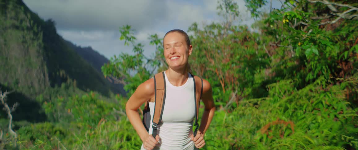 Awoman with a backpack hikes in a green mountain landscape