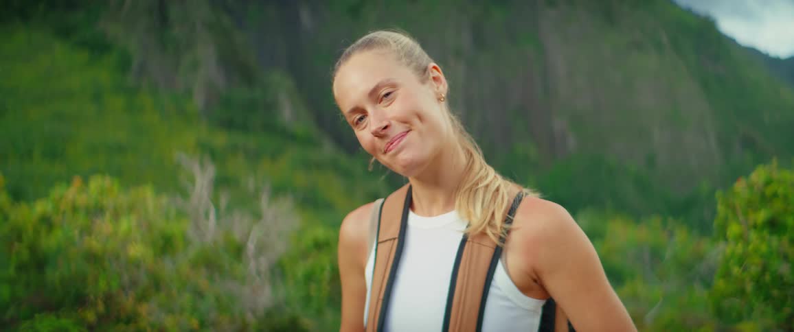 Smiling woman with a backpack poses on a trail surrounded by green mountains