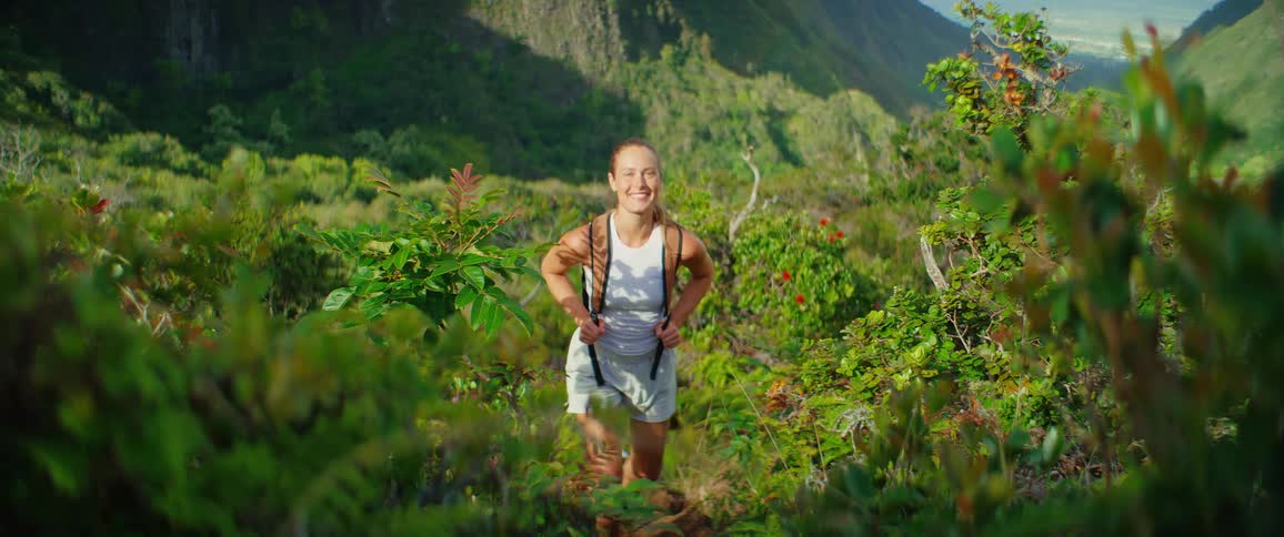 A woman hikes through lush green mountains on a sunny day