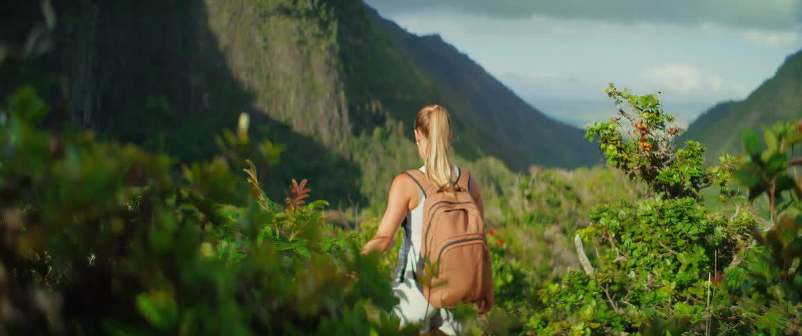 A young woman carrying a backpack hiking down a forested mountain area at midday