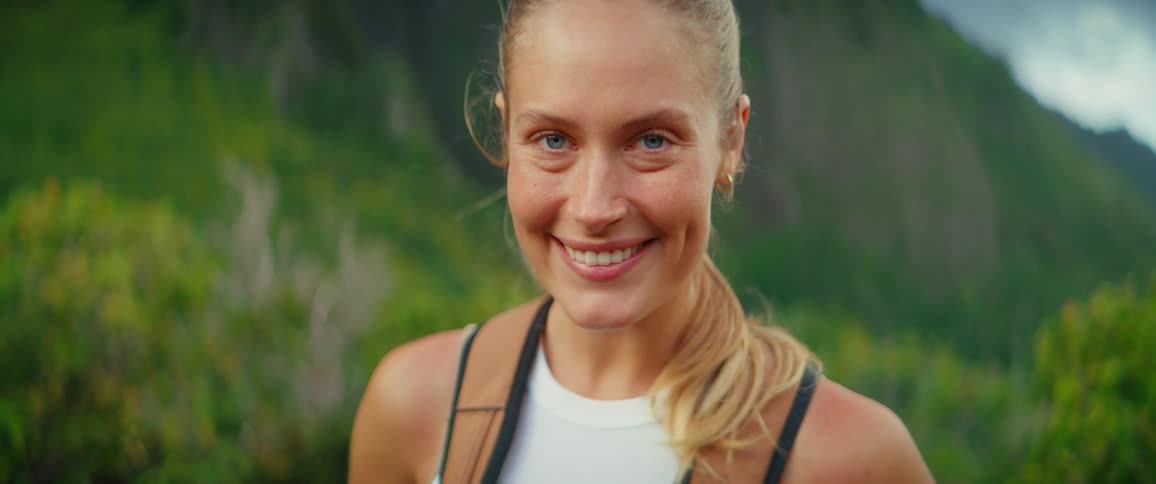 A young woman standing in the woods with a backpack during a hike at midday smiling