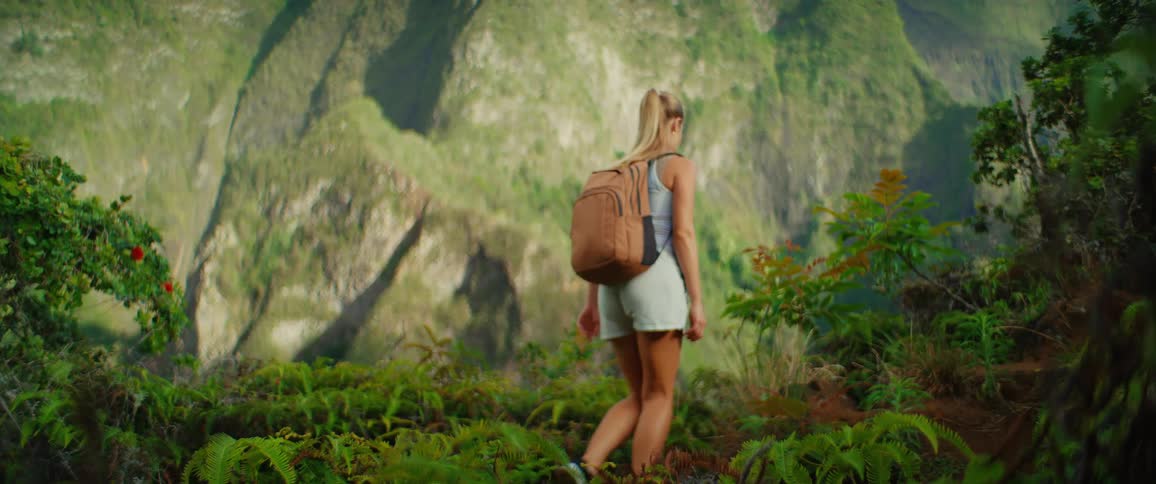 A woman with a backpack hikes along a lush green mountain trail