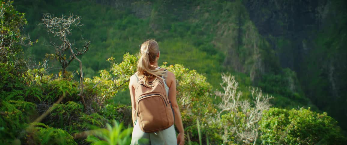 A happy woman with a backpack raises her arms in a forest