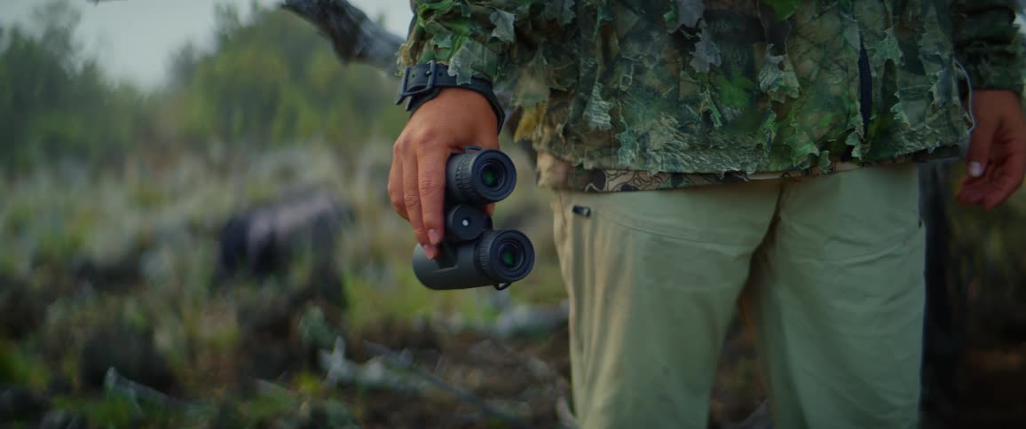The man lifts his binoculars in the grass