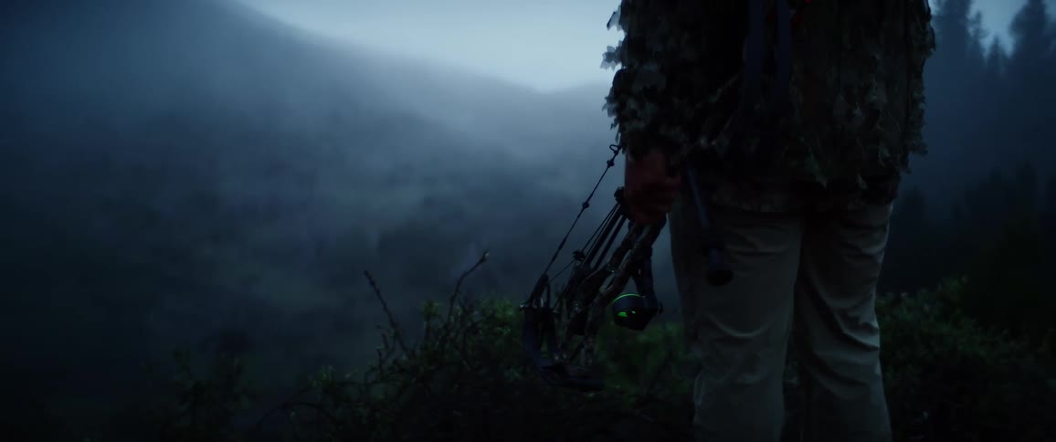 The hunter is standing on a hill with a bow in the fog