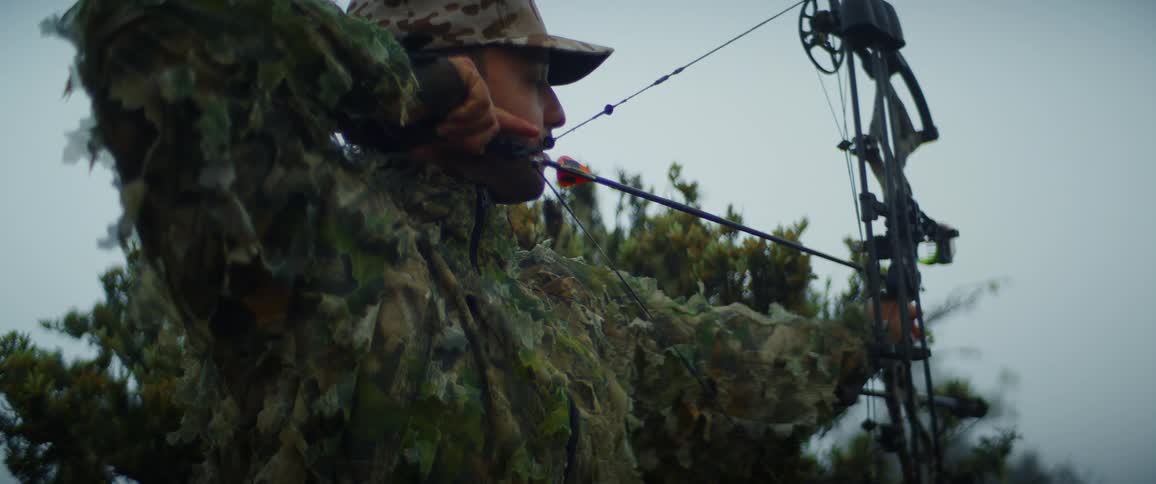 A man in camouflage is motionless while preparing to shoot an arrow with a bow
