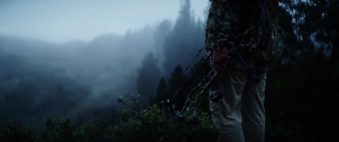 A man dressed in camouflage holds a bow while surveying his surroundings
