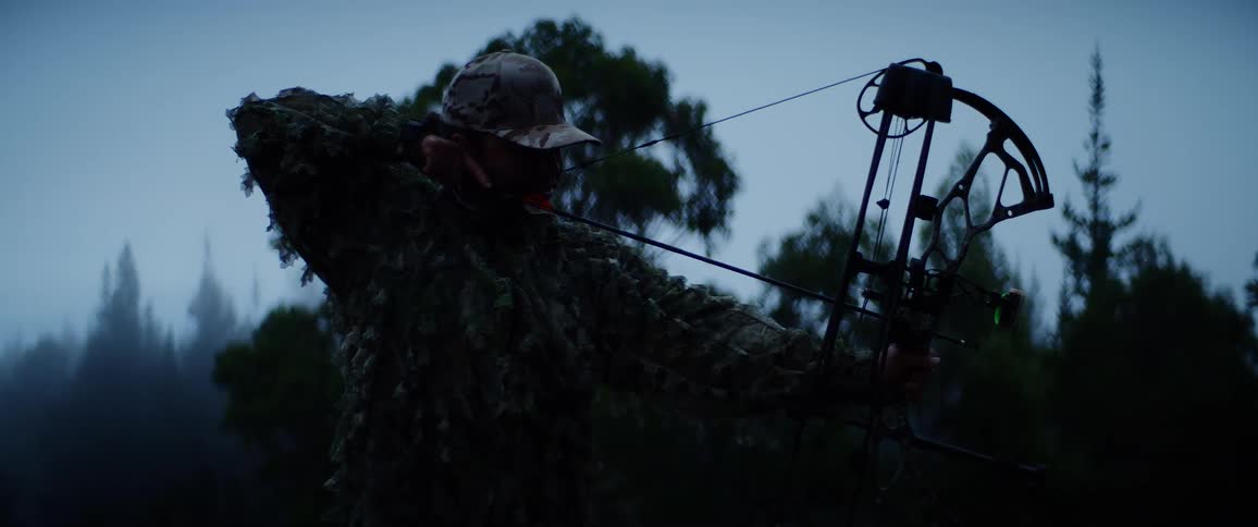 The main in camouflage aims a large bow
