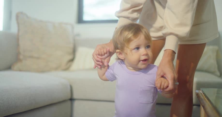 A mother holds her childs hands by the couch
