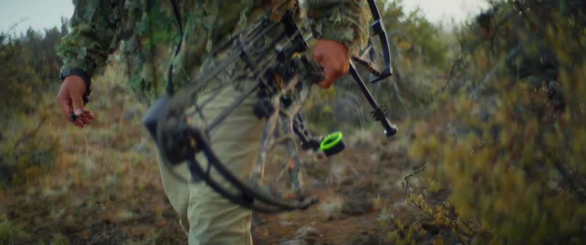 Camouflaged archer walks with a crossbow in a green environment