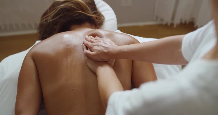 Woman receives back massages from a lady while laying on the massage bed