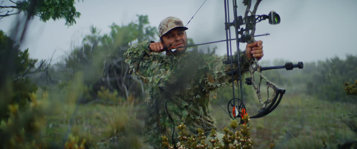 A man in the wild holding an arrow drawing his bow and taking aim for hunting