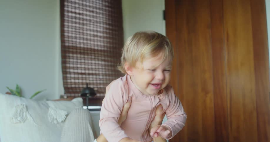 An adult woman is lying on a bed holding a little girl who is smiling on her lap