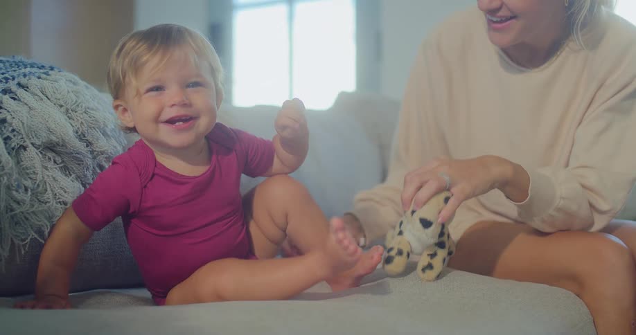 Child plays on the couch with her smiling mother beside her