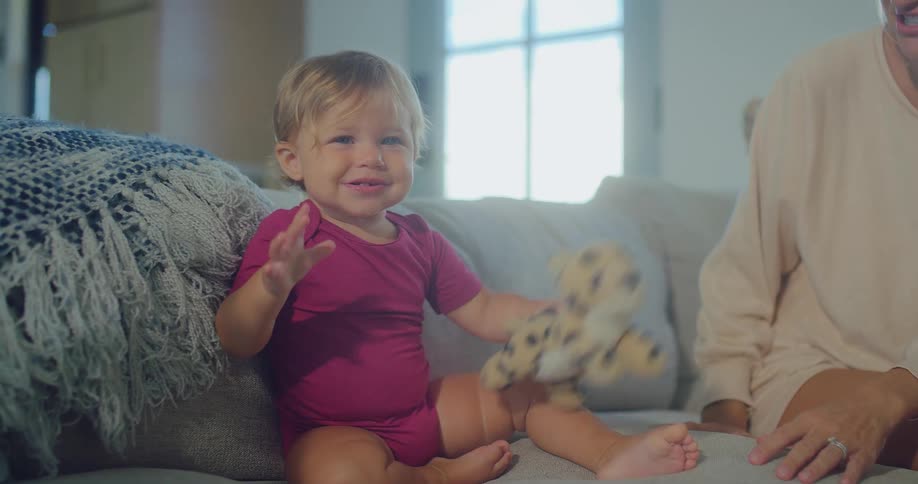 Happy baby playing with stuffed animal on couch as mom sits nearby