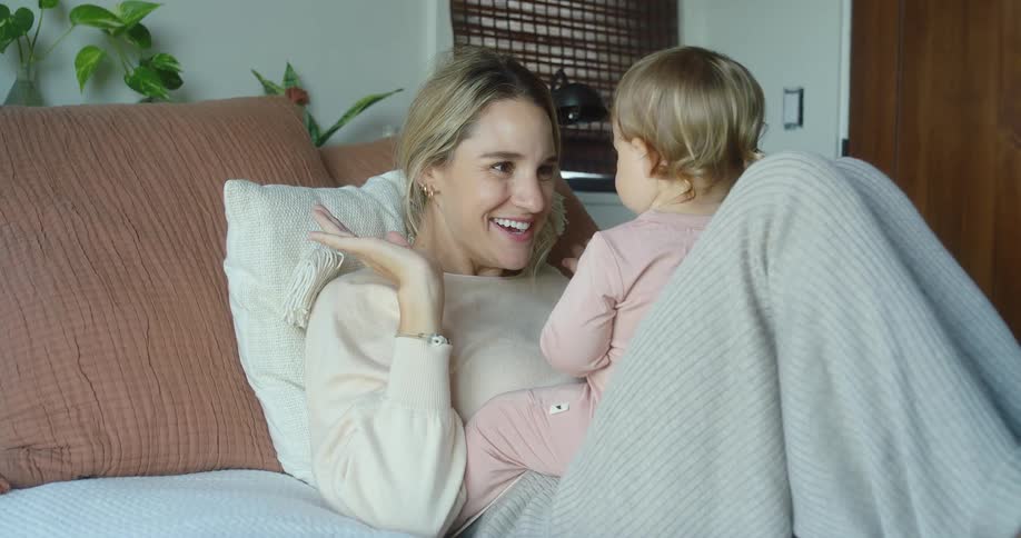 The video shows a woman and a baby playing peekaboo on a bed the woman covers and uncovers her eyes while the baby watches and they both smile and laugh as they play together