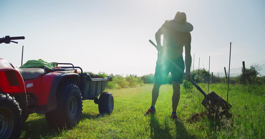 Shirtless male farmer with a hat on shoveling dirt outdoors during day time