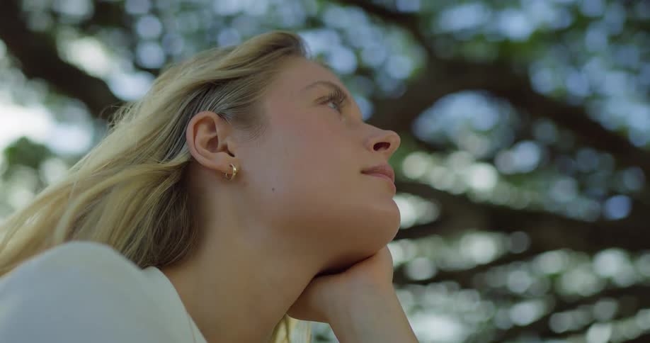Blonde woman rests her face on her hand while looking outdoors