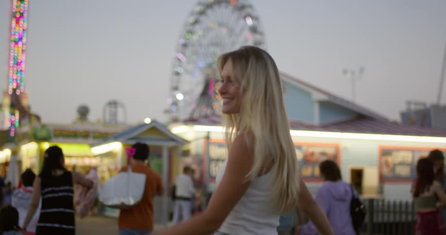 Woman smiles while walking through an amusement park at dusk