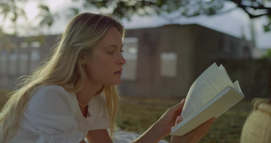 The woman lays on the picnic blanket reading