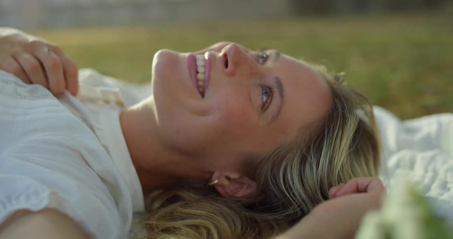 Laughing blonde female laying on her back on blanket outdoors