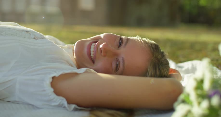 A woman smiles as she lays on her back on a blanket outdoors