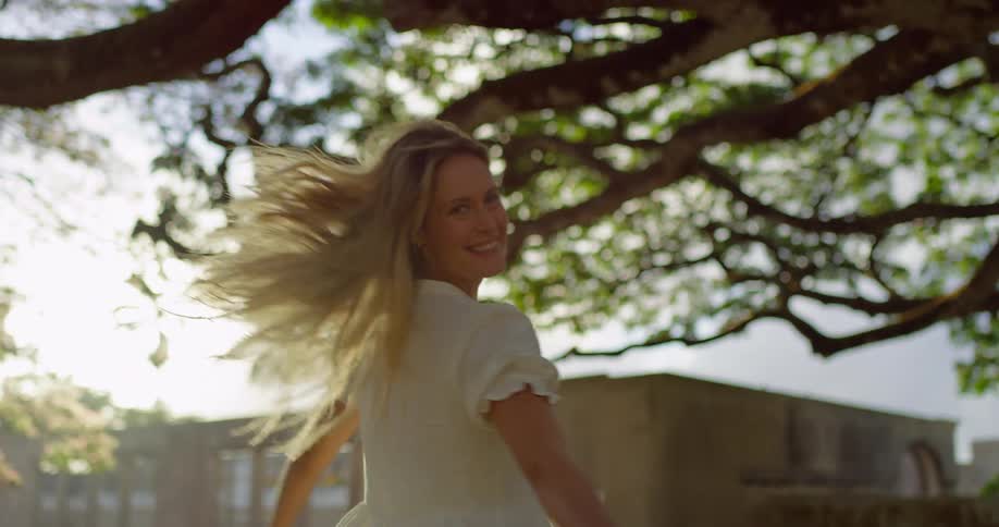 The woman spins and smiles under the tree