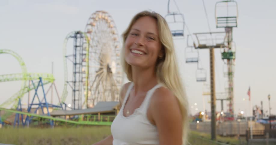Blonde woman smiles at amusement park with roller coaster in the background