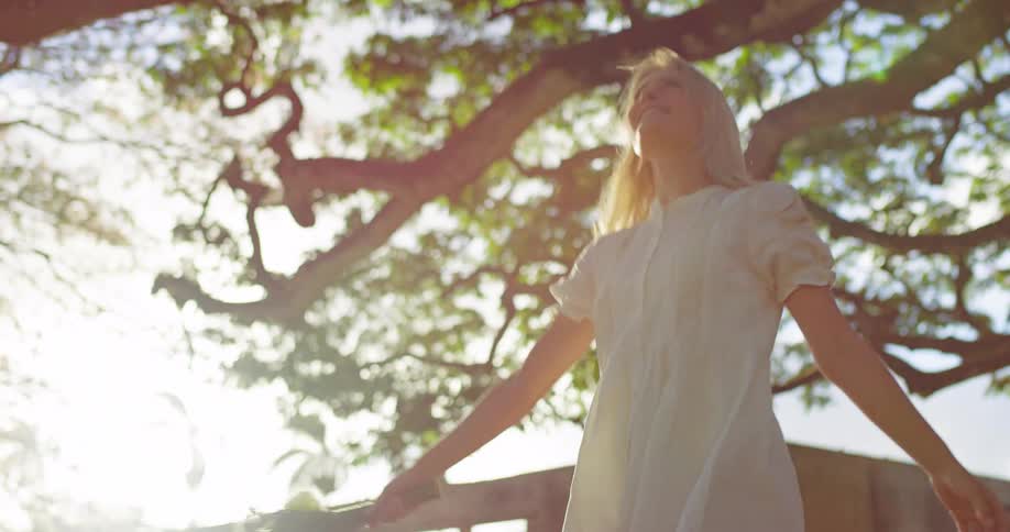 Woman in a white dress spins outdoors holding a bouquet of flowers
