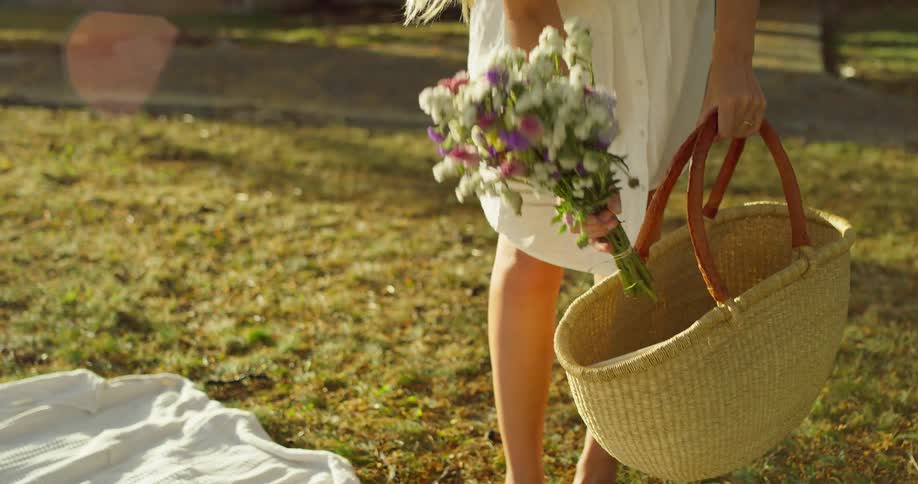 Woman arranges basket and book on a picnic blanket outdoors