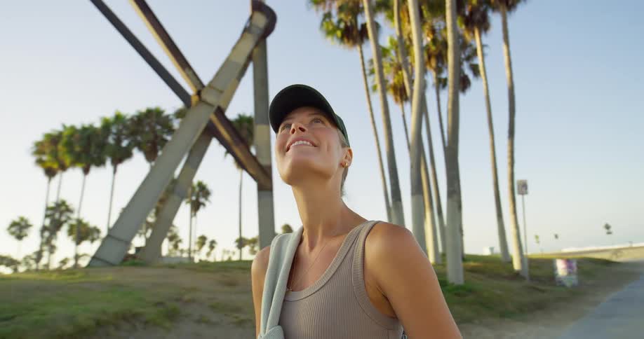 Bright optimistic close shot of a woman looking up as she stands at a palmlined beach area in warm evening light