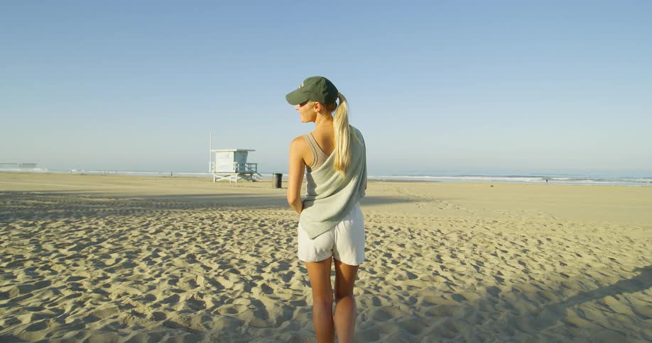 Woman wearing a cap walks on the beach sand on a sunny morning