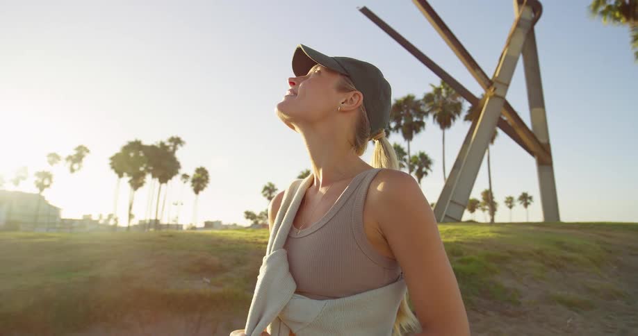 Blonde adult woman standing up and smiling on an asphalt road next to a beach watching the sunset outdoors