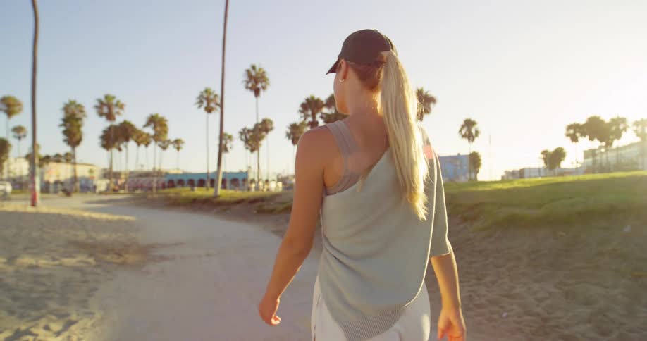 Woman walking on a beach boardwalk at sunset with palm trees in the background