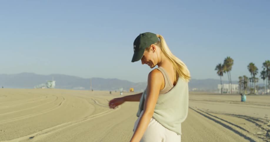 A woman walks happily along the sandy beach under a bright sunlight