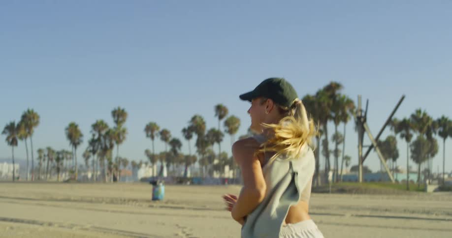Woman in cap walks on the beach sand with palm trees in the background