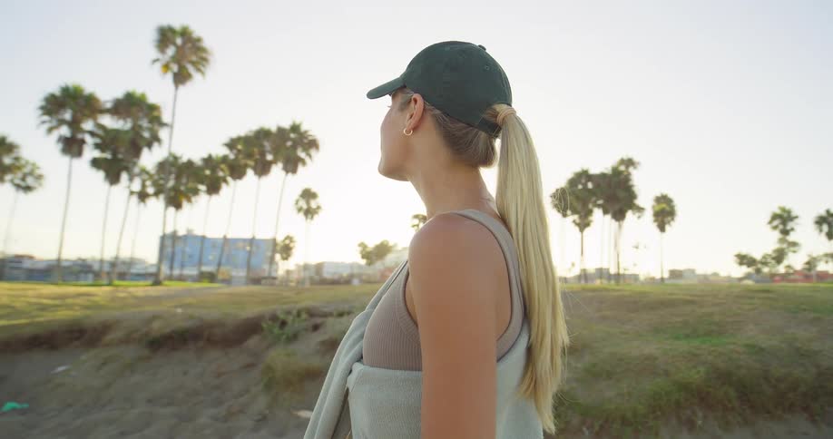 Woman in cap smiles outdoors with sunlit palm trees in the background