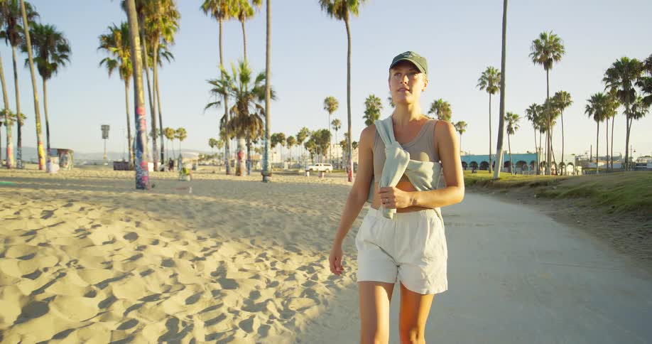 Woman walks along the beach surrounded by palm trees at sunset