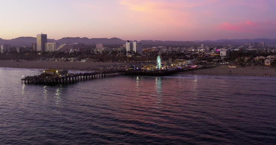 Aerial footage of a cityscape as it glows at dusk over water