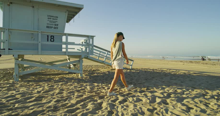 The woman is walking in the sand on a sunny day