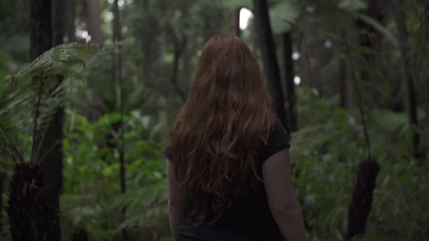 A woman walks into some dark woods