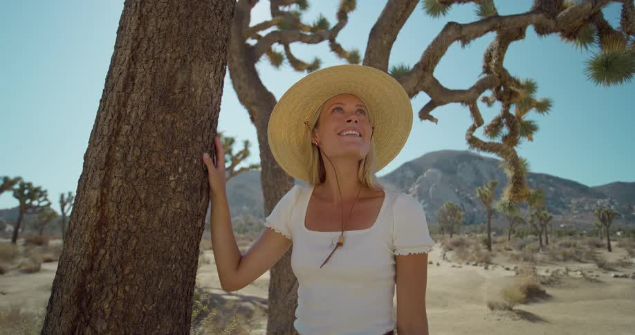 The woman smiles while leaning on a tree