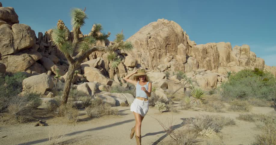 A young woman running in the wild under the sun wearing a hat with a rock formation in the background