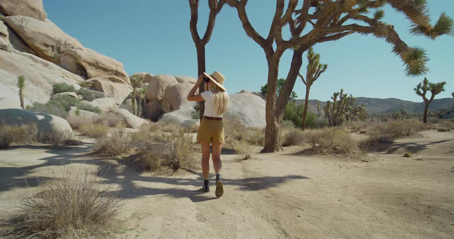 Woman with a hat walking along a desert trail with joshua trees and rocks