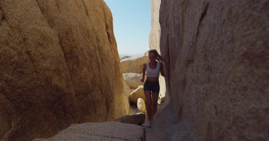 A young woman runs through a narrow rocky ravine on a sunny day
