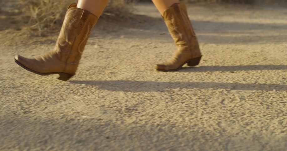 Close up of brown cowboy boots walking on a path in the desert